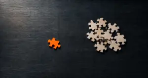 Piezas de puzle sobre una mesa oscura, una de ellas naranja y apartada del resto